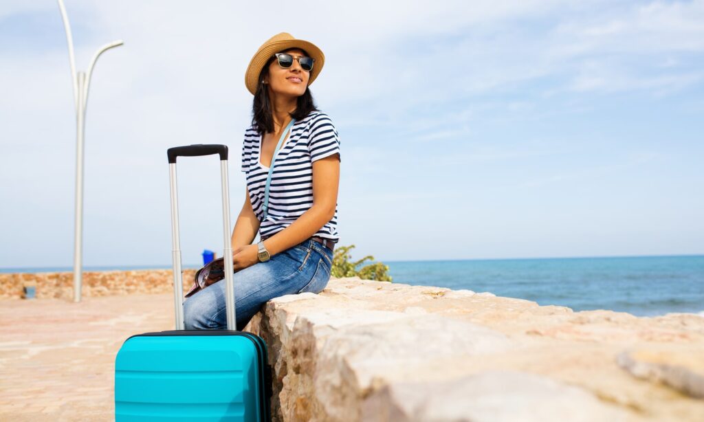 ung kvinde med kuffert og solhat i udlandet